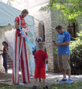 A man on stilts makes balloon animals for children